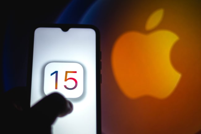 Smartphoneskärm med iOS 15-logotypen och Apples logotyp i bakgrunden.