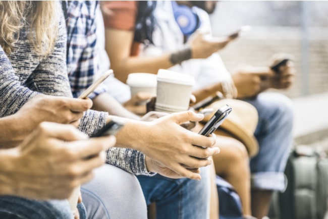 Närbild på människor som sitter bredvid varandra med mobiler och kaffe i händerna.