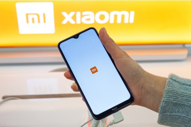 Hand håller upp xiaomi-mobil, med xiaomis logga i bakgrunden.