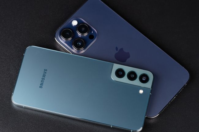 Samsungmobil ligger ovanpå iphone mot svart bakgrund.